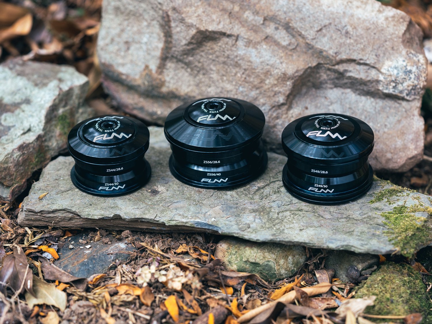Three black Funn bicycle headsets are arranged on a flat rock outdoors, surrounded by leaves and larger stones. The headsets, each labeled with Funn, vary in height and are positioned from shortest to tallest left to right.