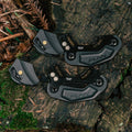 Two black Funn Zippa LG Chain Guides, CNC-machined from alloy, rest on a mossy tree stump surrounded by greenery and leaves in a forest—perfect for high-pivot bikes.