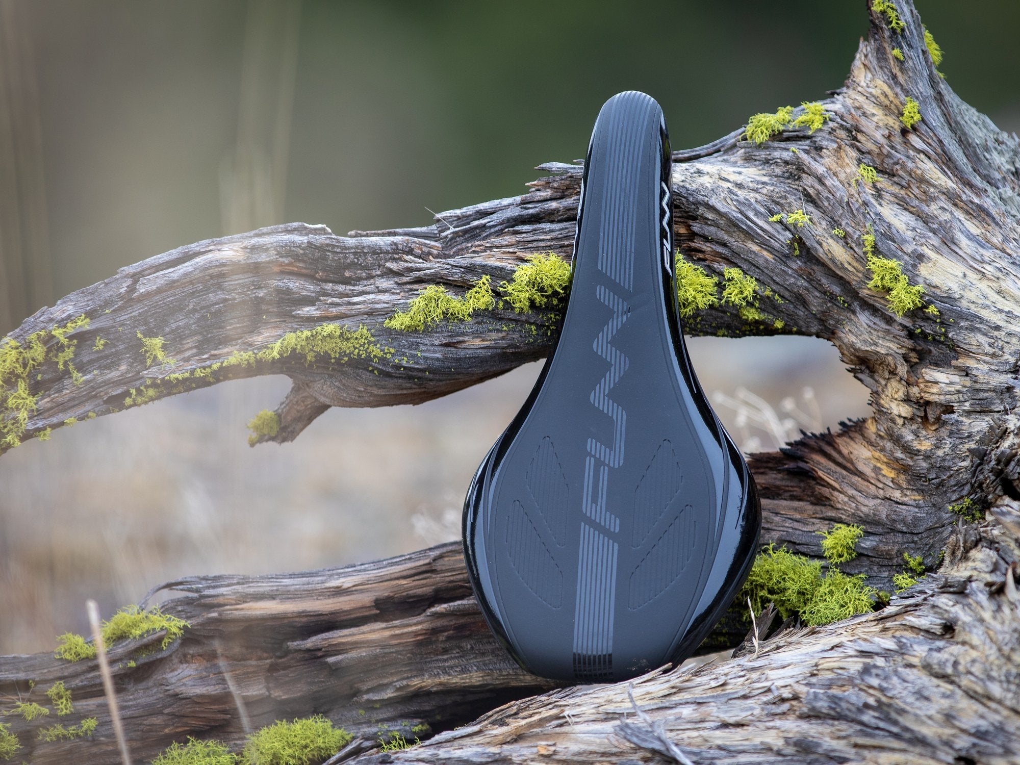 a sleek Funn saddle placed on a rugged, moss-covered piece of wood in an outdoor setting, emphasizing its connection to nature and performance in demanding conditions.