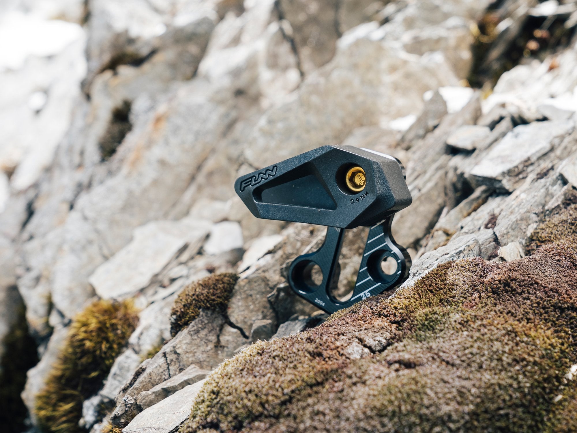 A close-up of a Funn zippa lite e-type chain guide resting on rugged, moss-covered rocks in an outdoor setting.