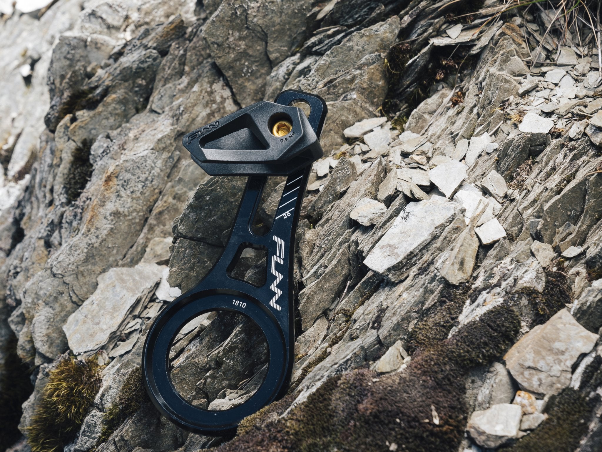 A close-up of a Funn zippa lite bsa chain guide resting on rugged, moss-covered rocks in an outdoor setting.