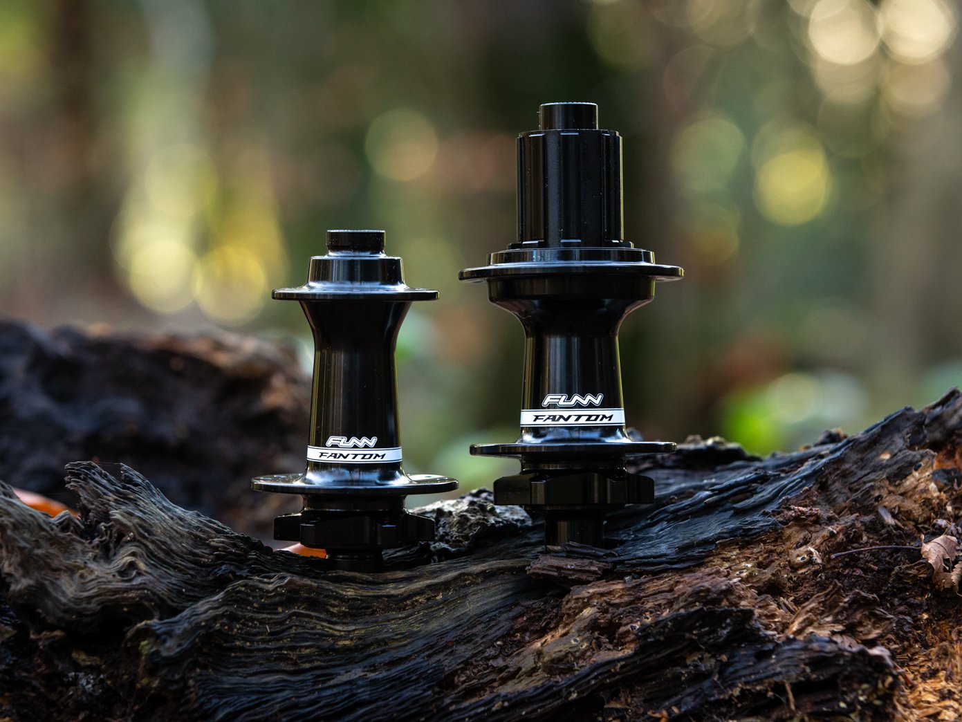 two Funn Fantom hubs placed on a natural wooden surface, possibly a log, set against a blurred forest backdrop.