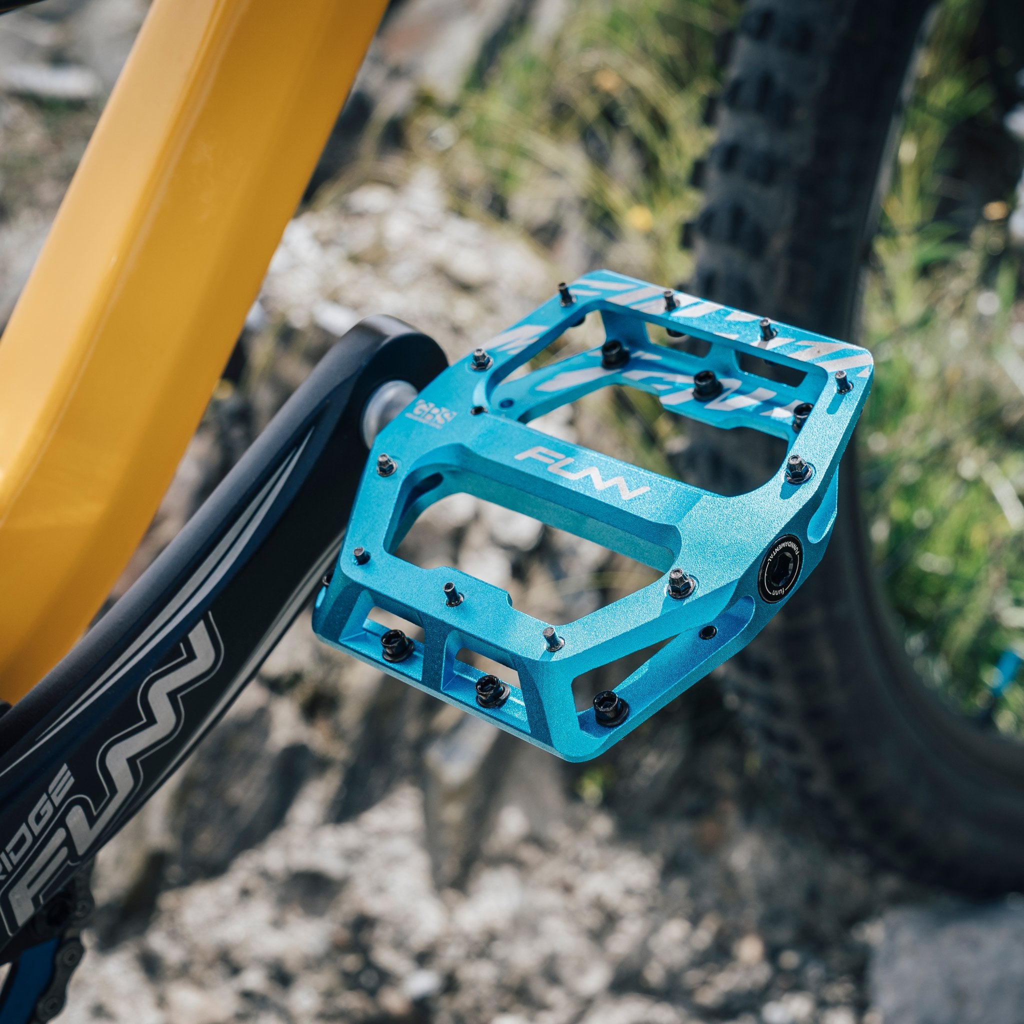 A Funn Funndamental flat bike pedal in turquoise color on a yellow bike