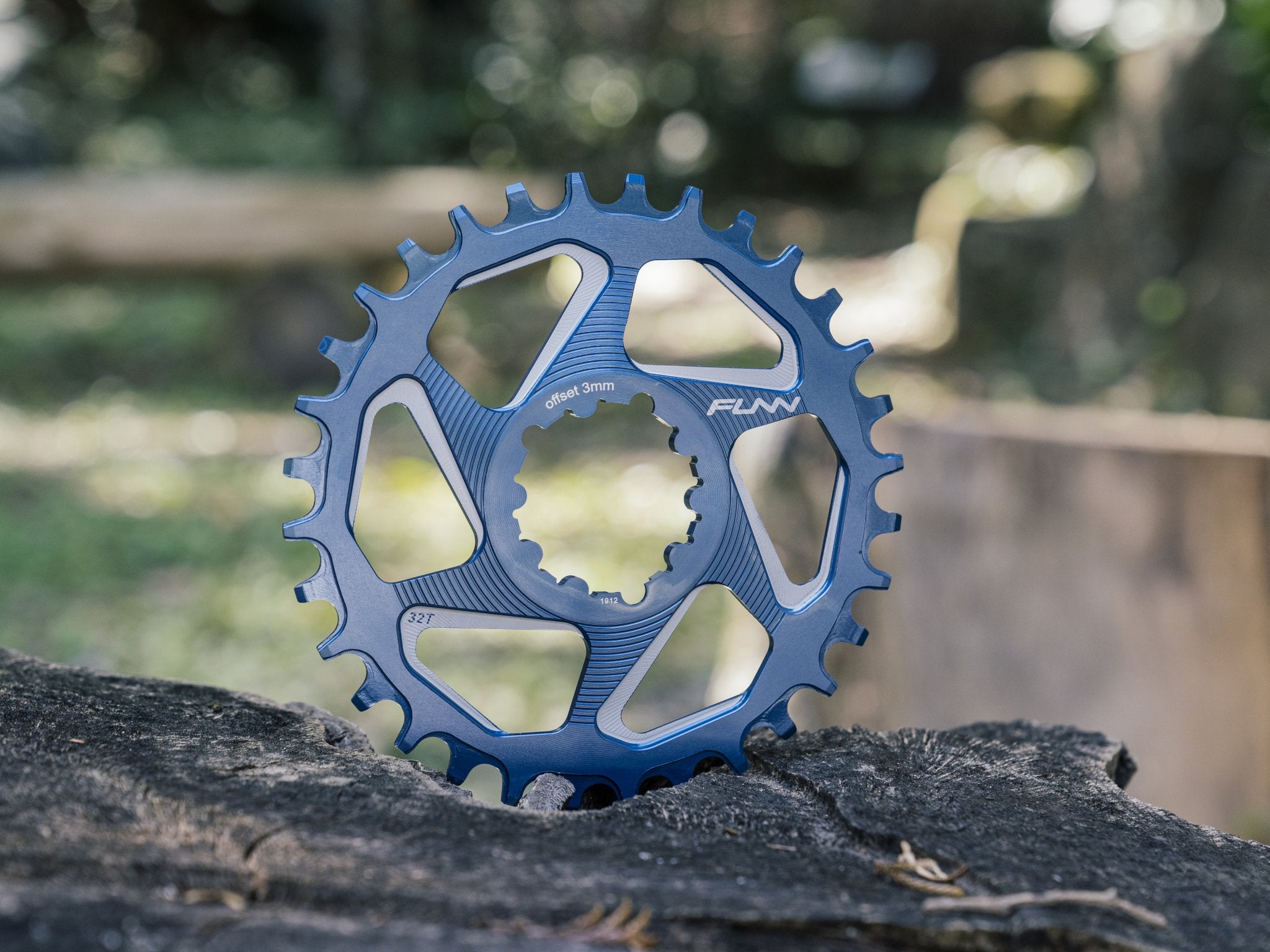 This image features a blue Funn solo dx chainring standing vertically on a rugged surface, set against a blurred outdoor background. 