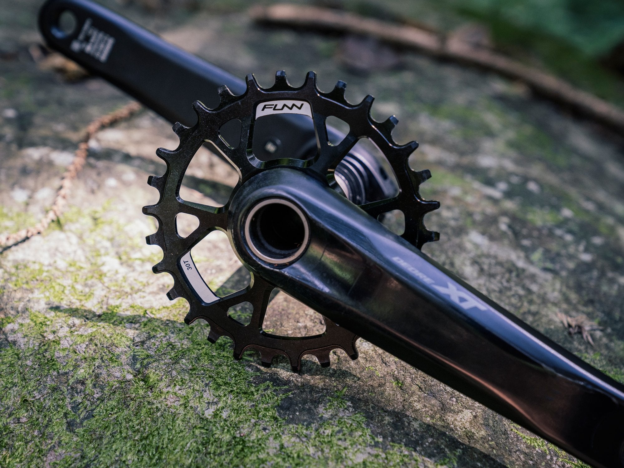 This image displays a crankset featuring a black funn solo ds chainring, placed against a rocky, natural backdrop.