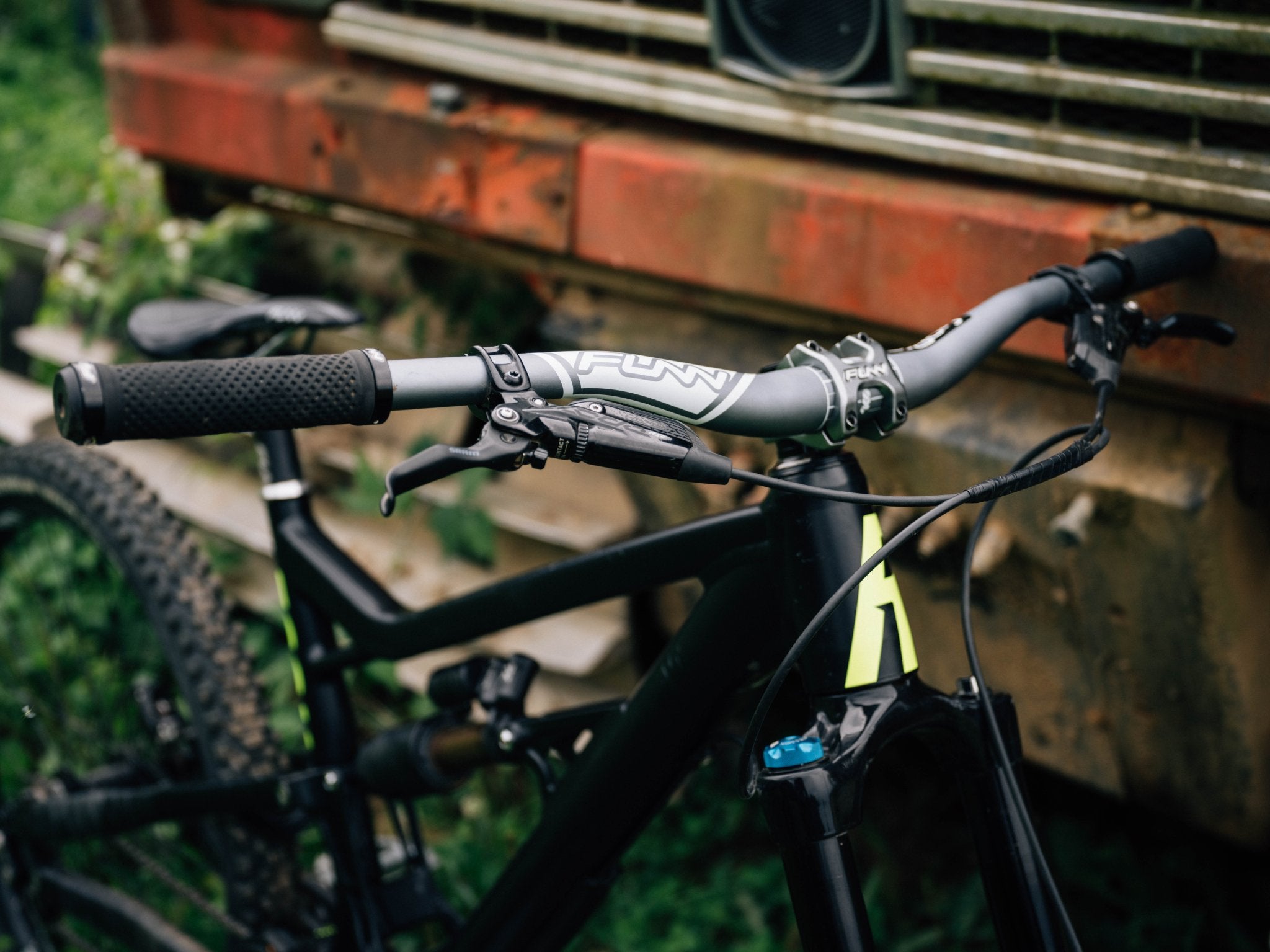 a mountain bike equipped with funn components of a gray kingpin handlebar, crossfire stem and black combat i grips stands beside a truck