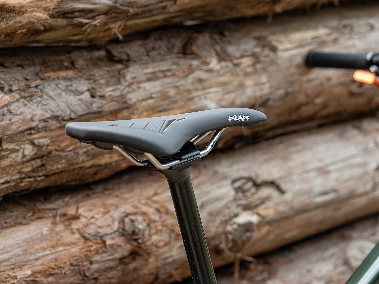 Funn skinny bike saddle securely mounted on a seat post, set against a rustic background of stacked logs.