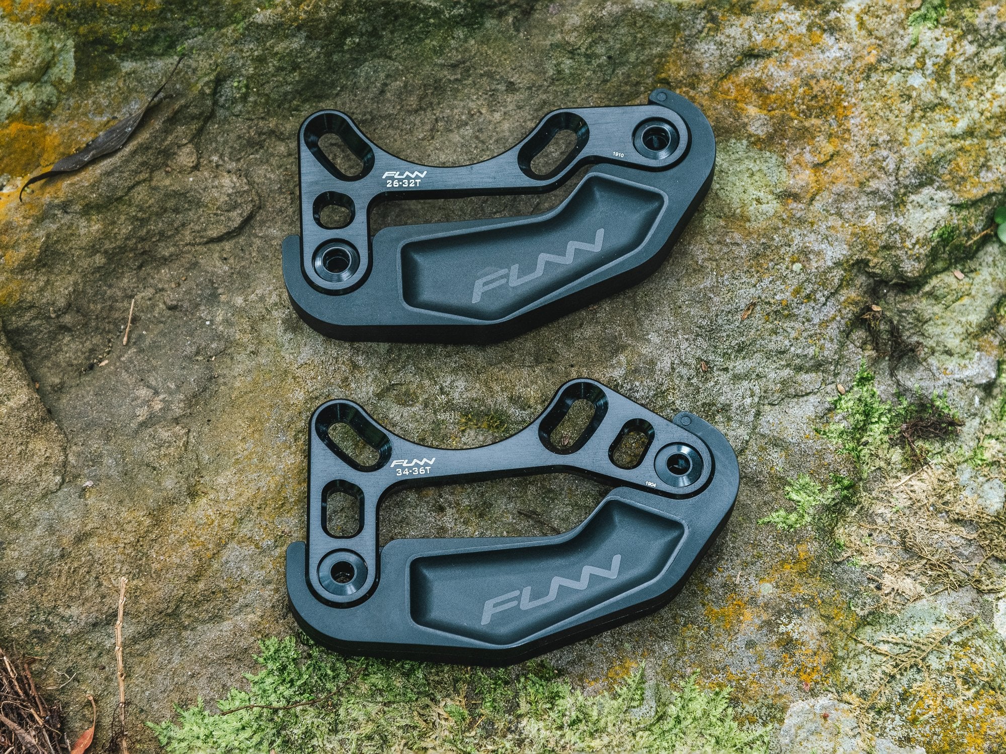 Two black Funn zippa bash guards are displayed on a textured rock surface, each labeled with the compatible chainring sizes of 26-32T and 34-36T.