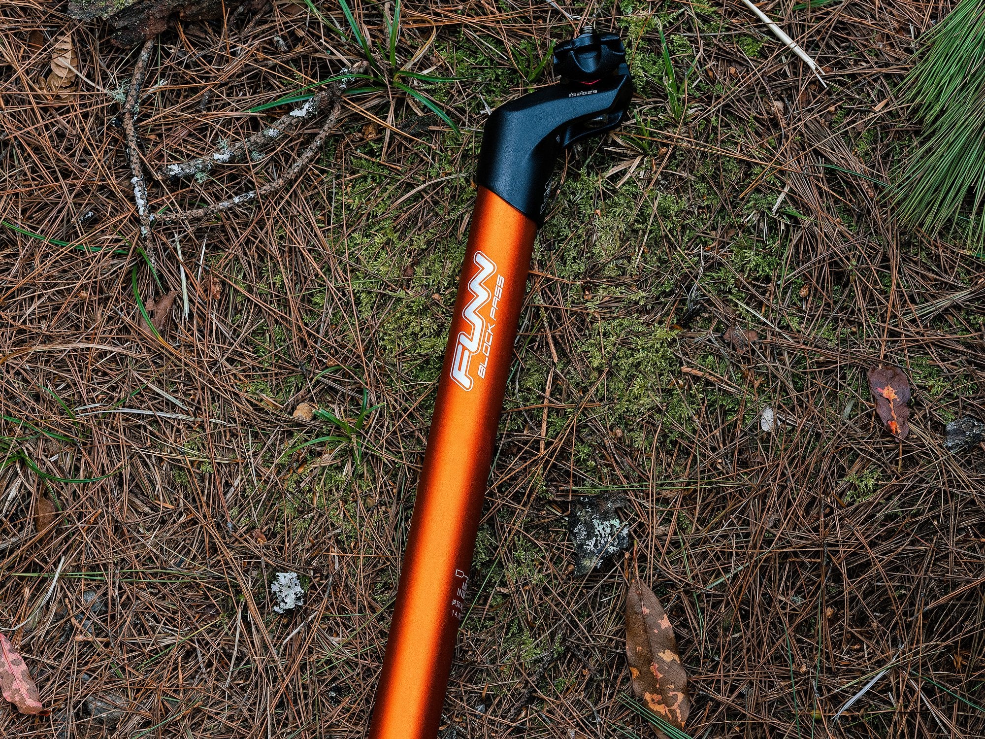 The image displays an orange Funn blockpass seat post arranged in a row on a forest floor covered with pine needles.