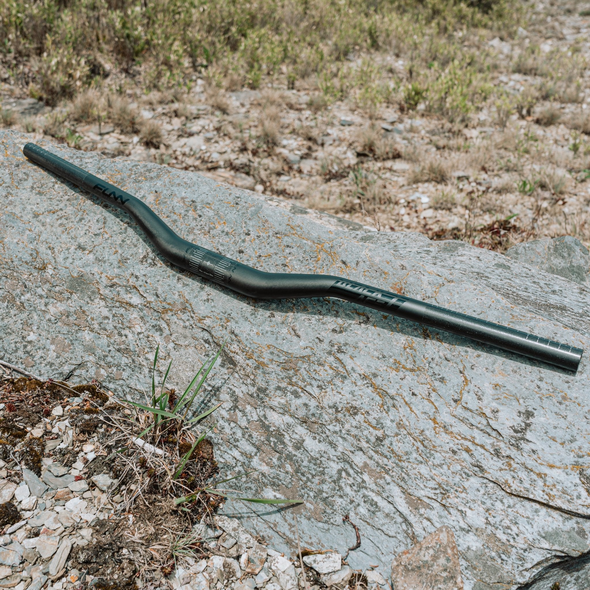 FUNN Black Ace carbon handlebar, matte black riser bar with slight sweep for mountain bikes, shown on rocky outdoor terrain