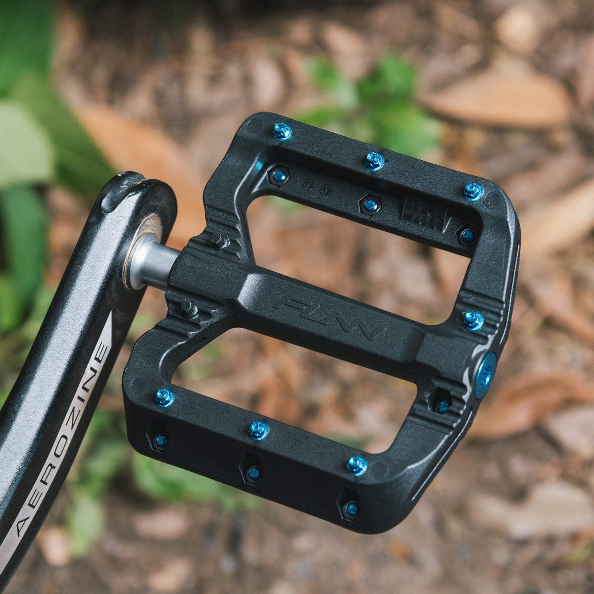 Black Magic Flat Pedals by FUNN, black composite pedal with blue pins on bike crank, wide platform for MTB grip and control