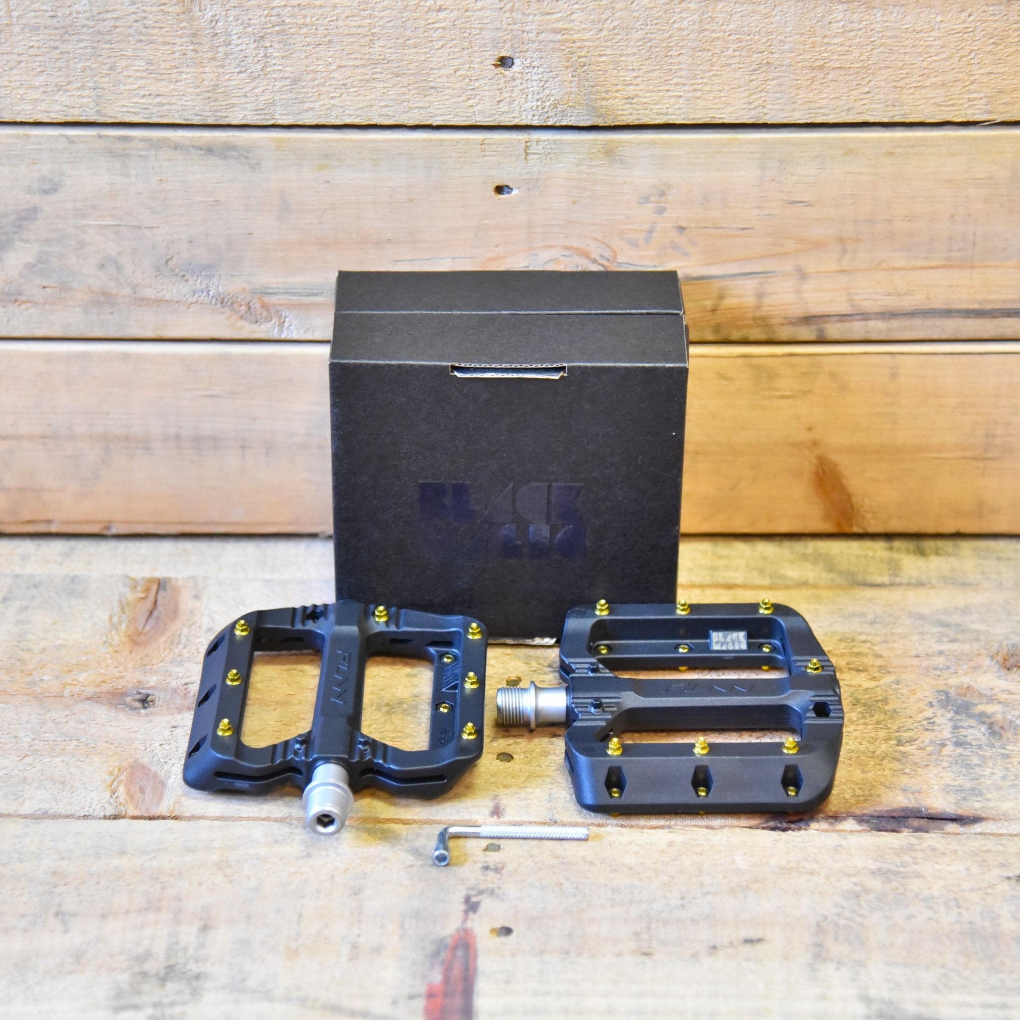 FUNN Black Magic Flat Pedals composite pedal set with gold pins and pin tool on wood surface, durable MTB bike platform