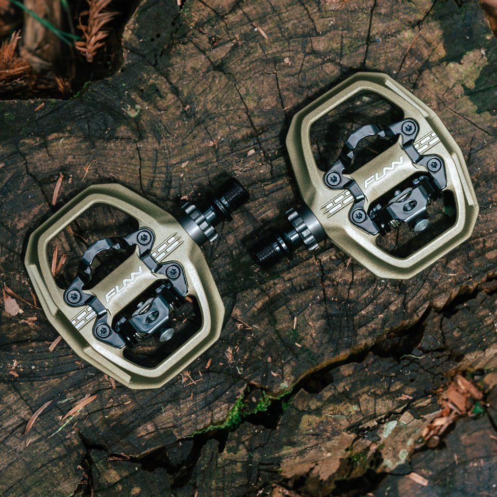 FUNN Clast Clip-In Pedals, in pilsner, alloy MTB pedals with wide platform and SPD-style clip mechanism on tree stump.