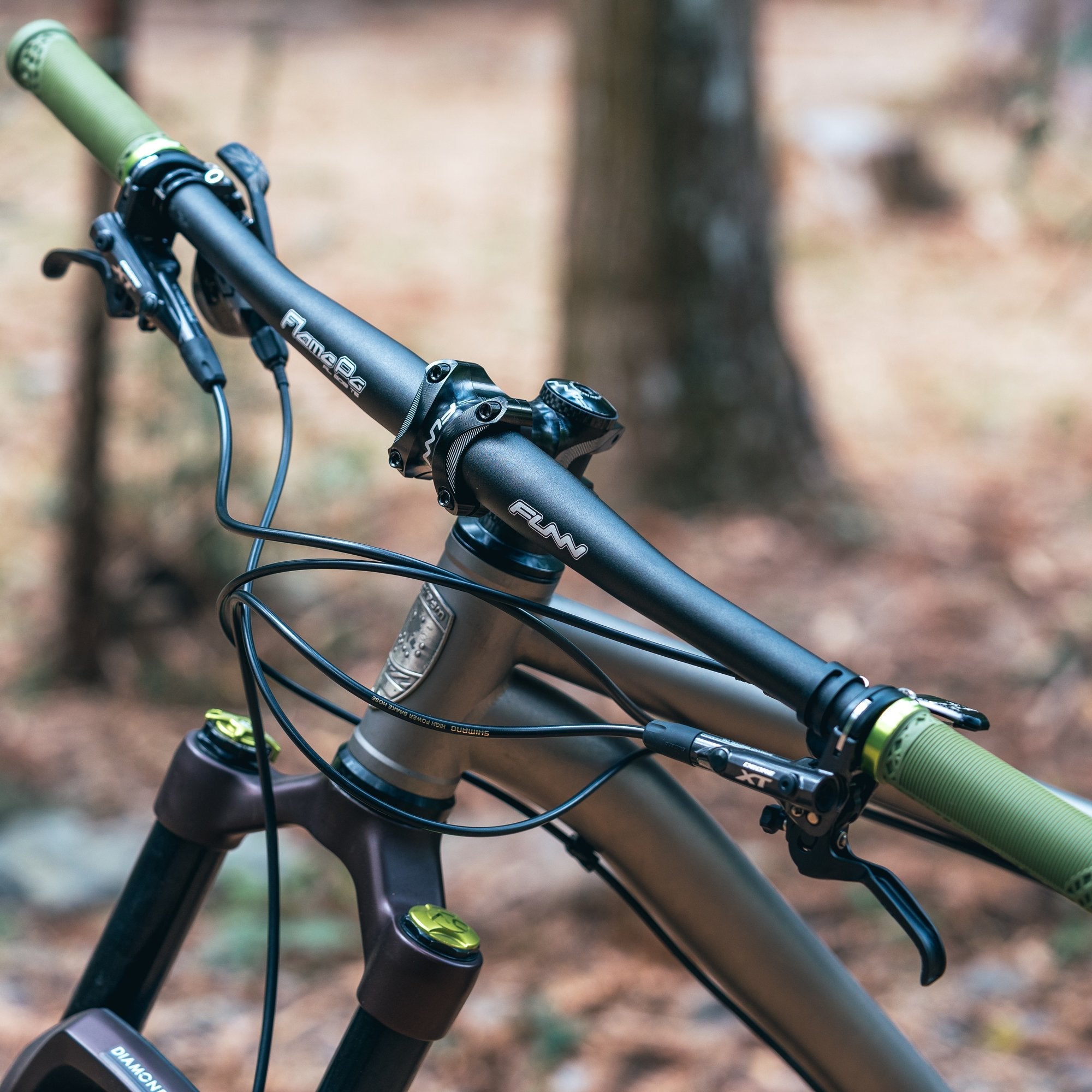 FUNN Flame Pg Flat Handlebar 710mm, black alloy bar with green grips on XC trail mountain bike in forest setting