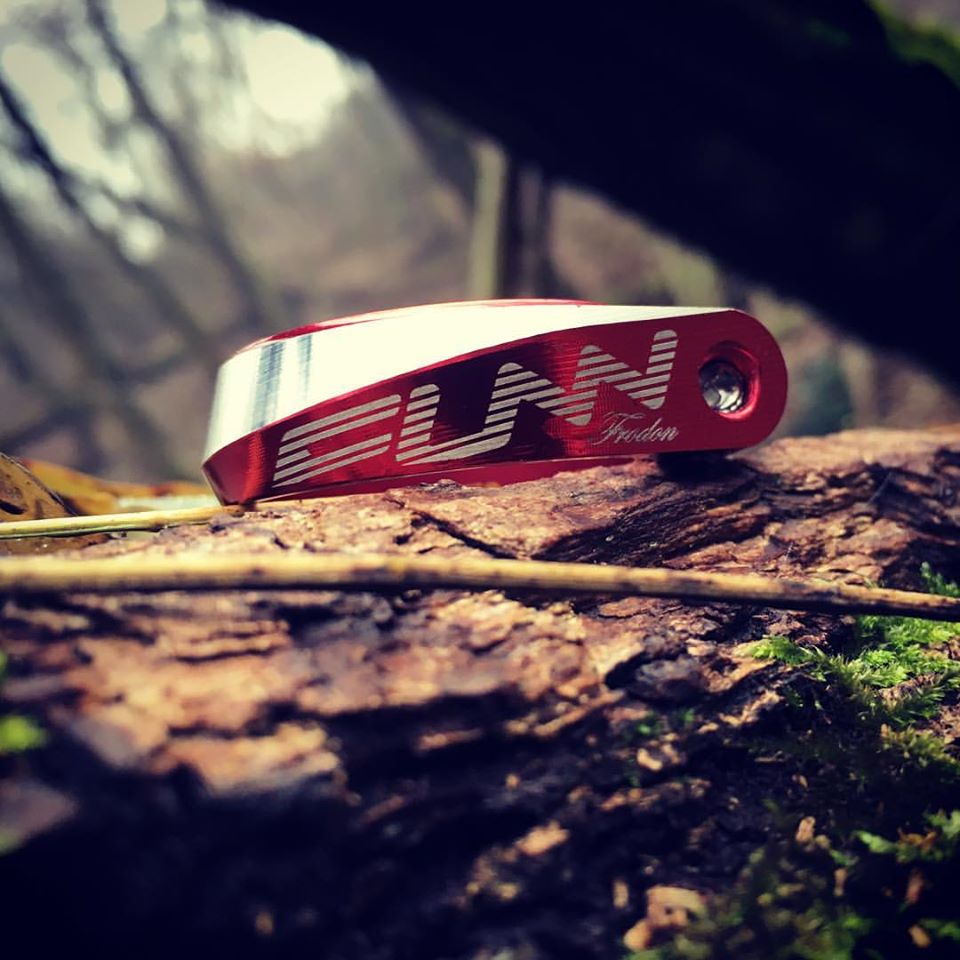 Red and silver FUNN Frodon Seat Clamp, CNC-machined alloy bike seatpost clamp resting on a log in the forest.