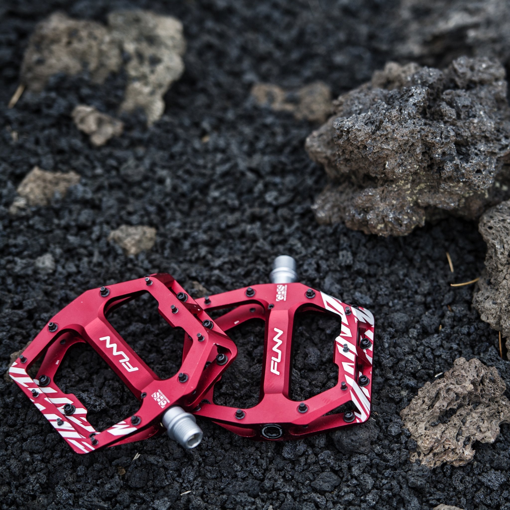 Red FUNN Funndamental flat pedals with alloy body and traction pins, low-profile MTB platform on rugged black rock background