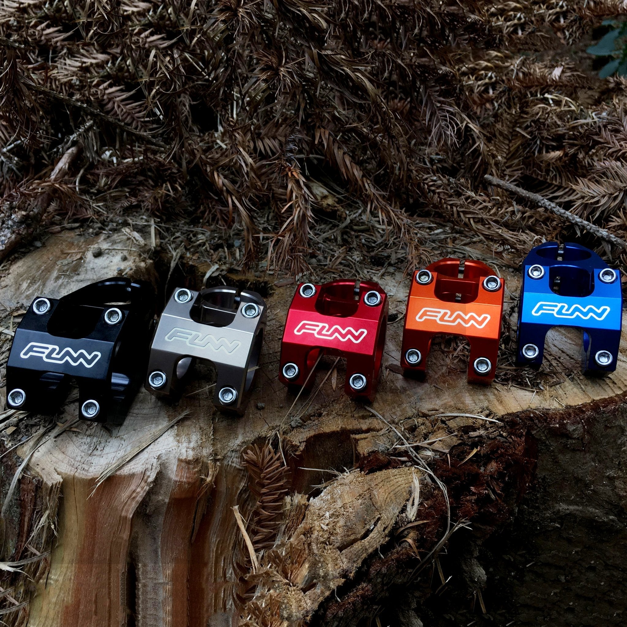 FUNN Funnduro Stem, CNC alloy mountain bike stem in black, silver, red, orange and blue, shown on a tree stump outdoors