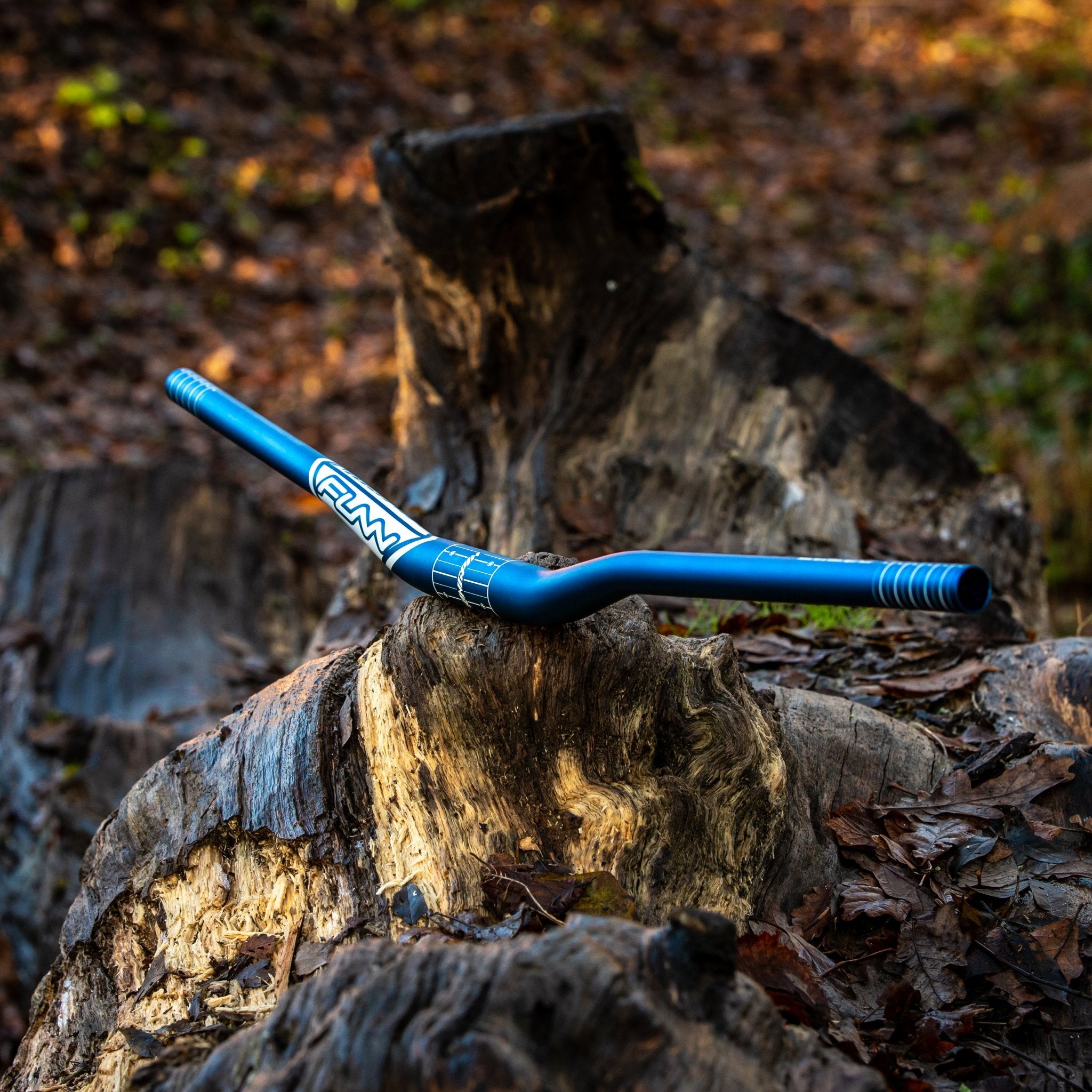 Blue FUNN Kingpin Riser Handlebar, lightweight alloy MTB bar with upsweep and backsweep, shown on a forest log outdoors