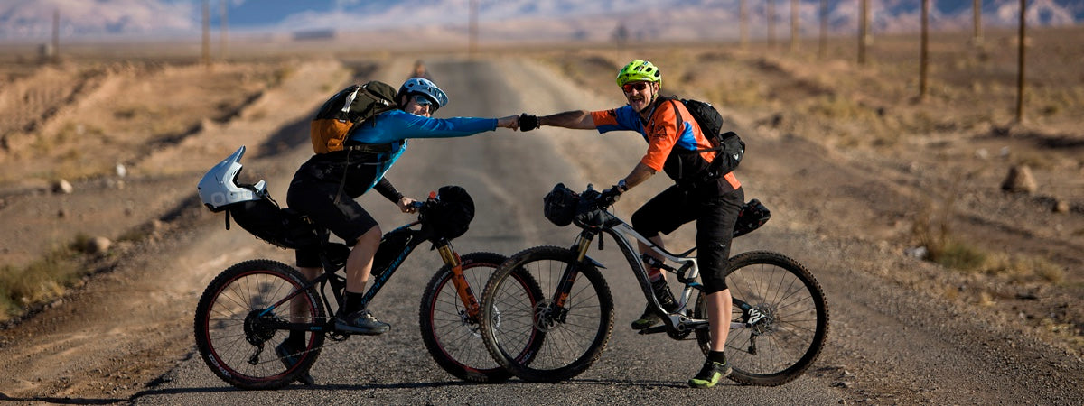 two funn riders cheer to each other in front of a mountin view