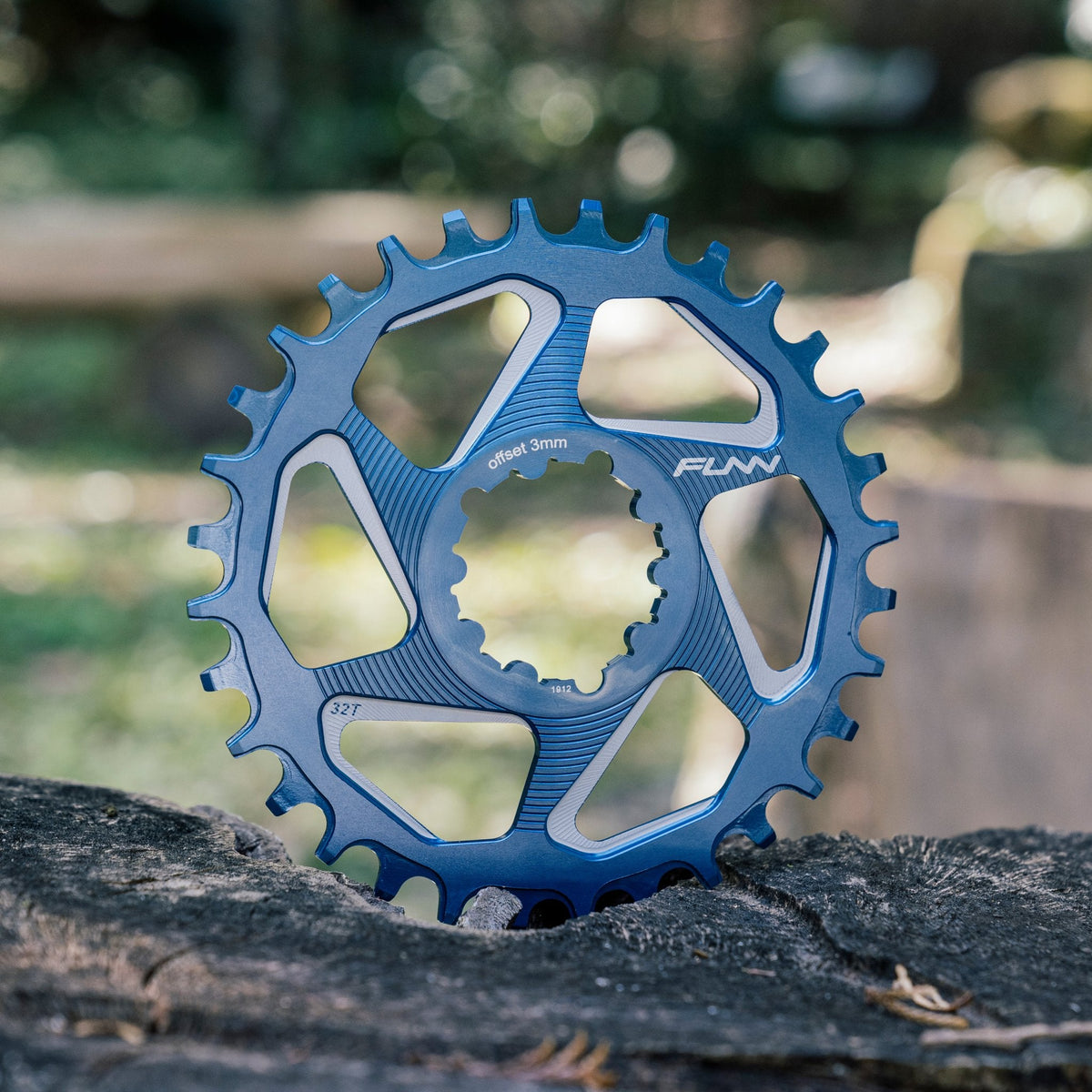 FUNN Solo DX Narrow-Wide Chainring, blue alloy MTB chainring with 3mm offset and 32T teeth, resting on a tree stump outdoors