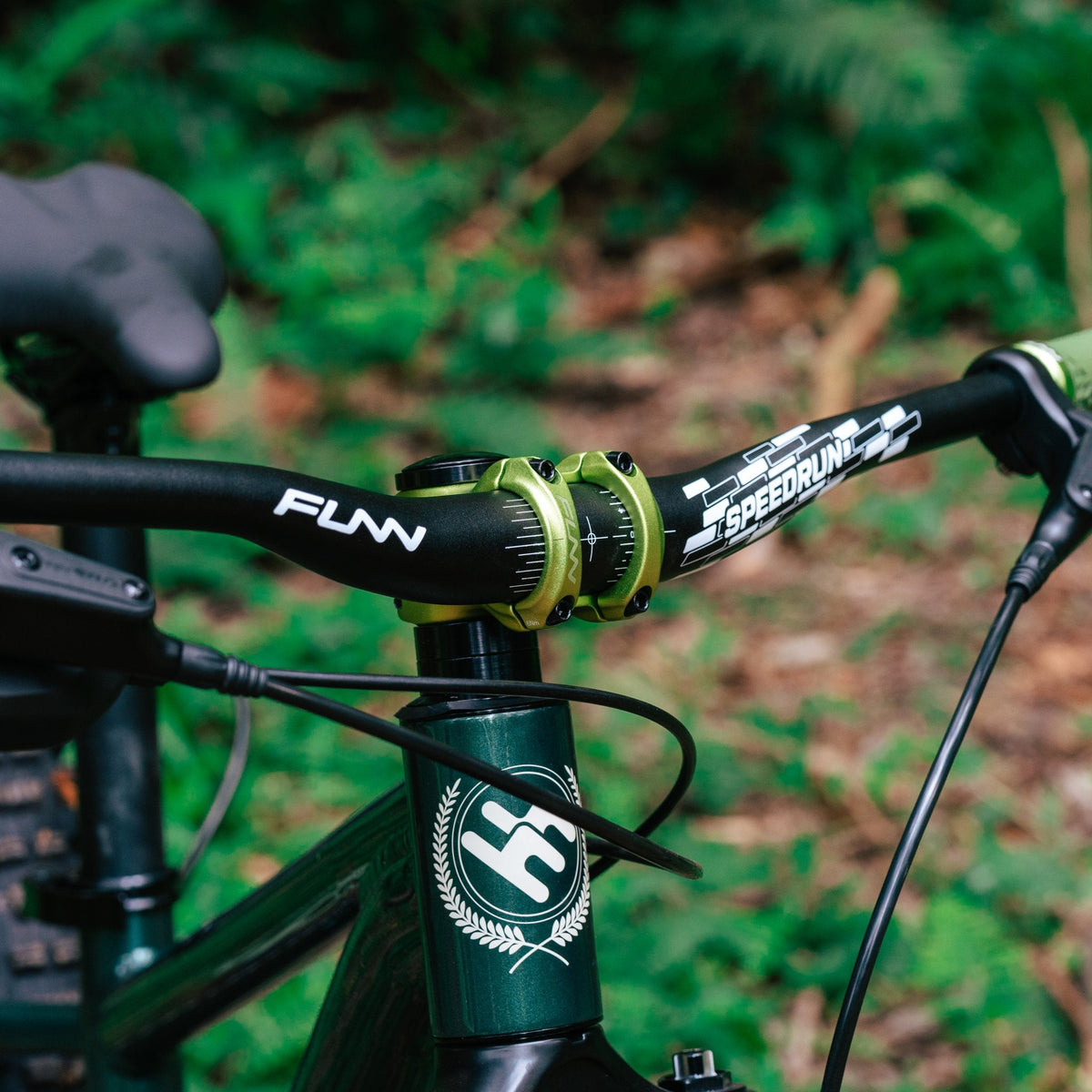 FUNN Speedrun Junior Handlebar, black alloy youth MTB bar with green stem clamp, mounted on a trail bike in the forest