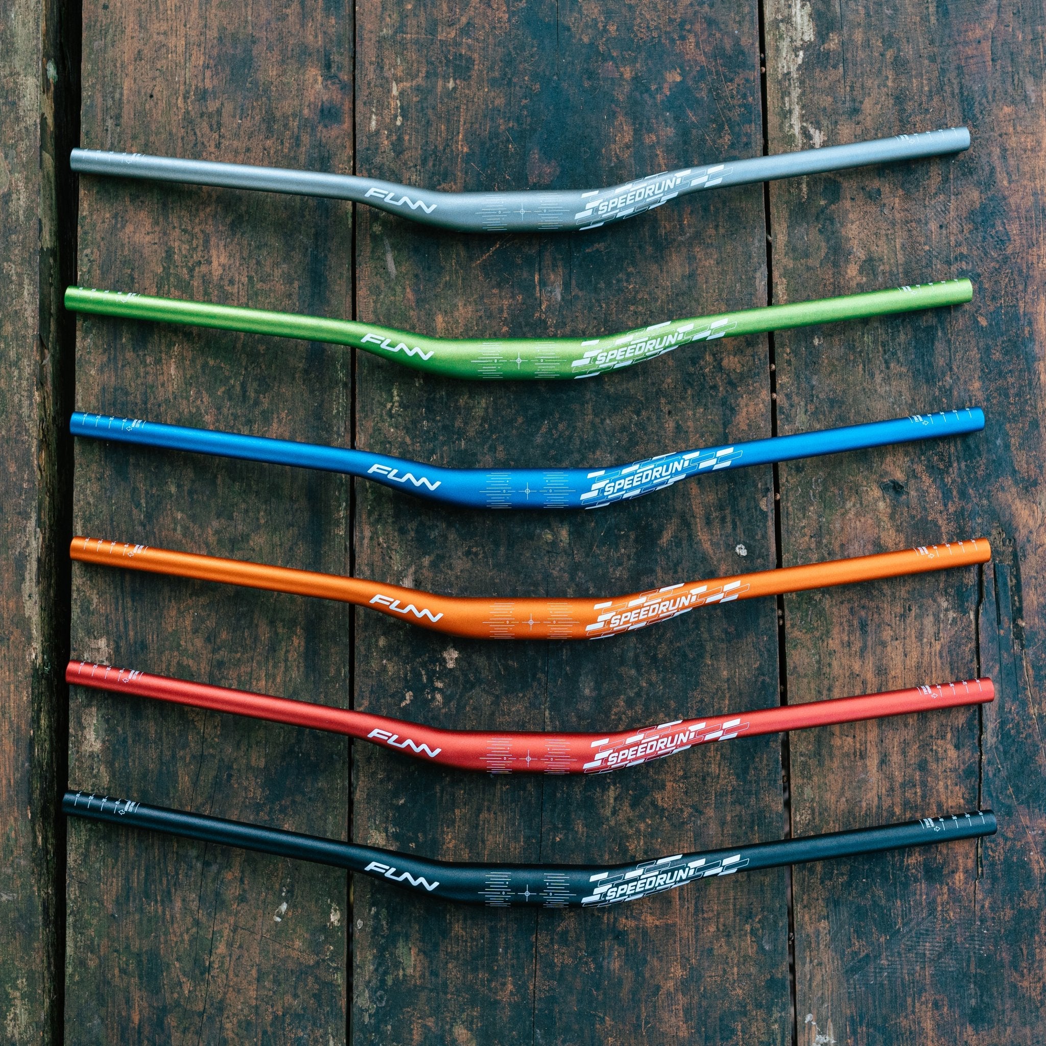 FUNN Speedrun Junior Handlebar range in alloy, colorful riser bars for kids’ mountain bikes laid out on rustic wood background