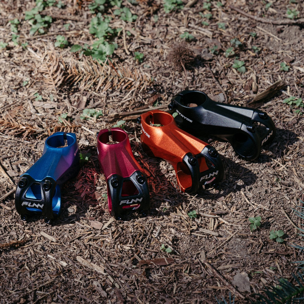 FUNN Stryge Drop Stem in blue, red, orange and black alloy, short MTB handlebar stems laid on outdoor trail ground