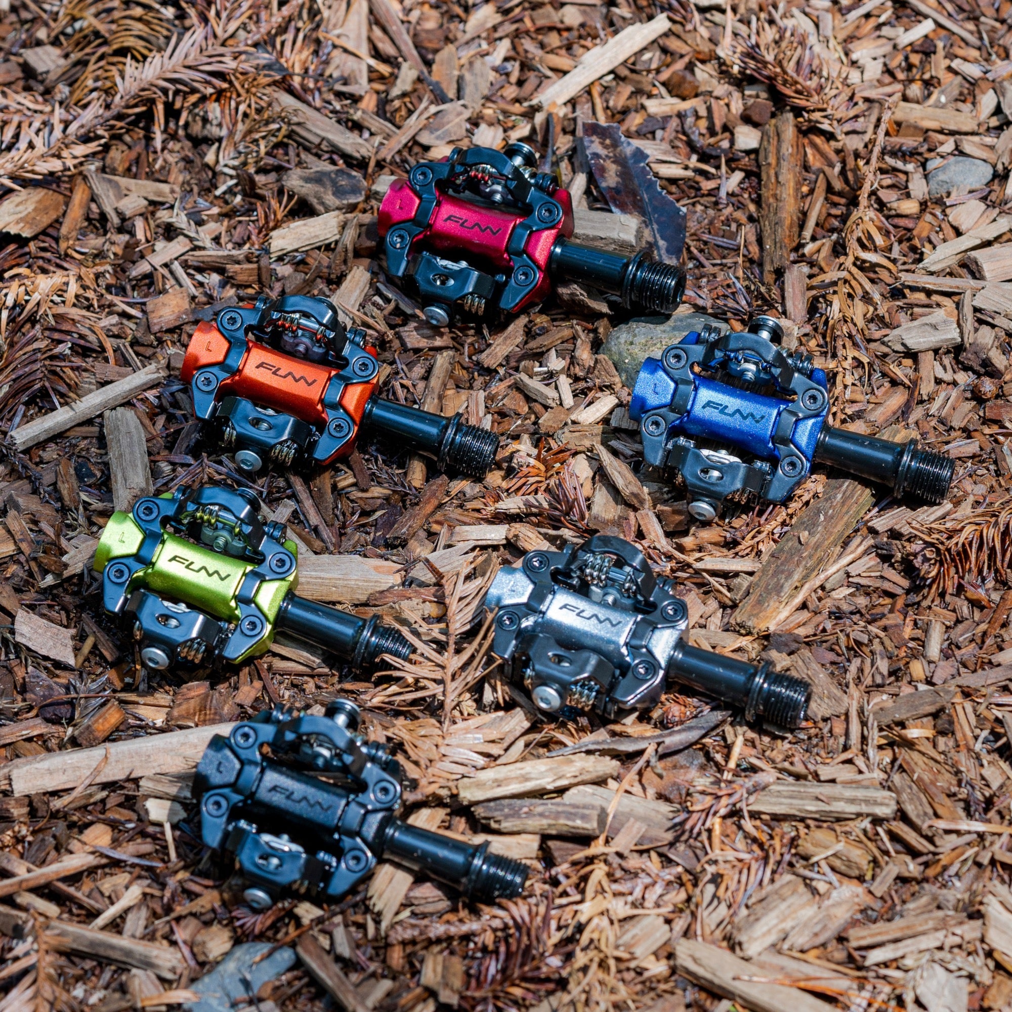 FUNN Tactic Clip-In Pedals in colorful anodized alloy, dual-sided SPD-style bike pedals displayed on forest trail mulch