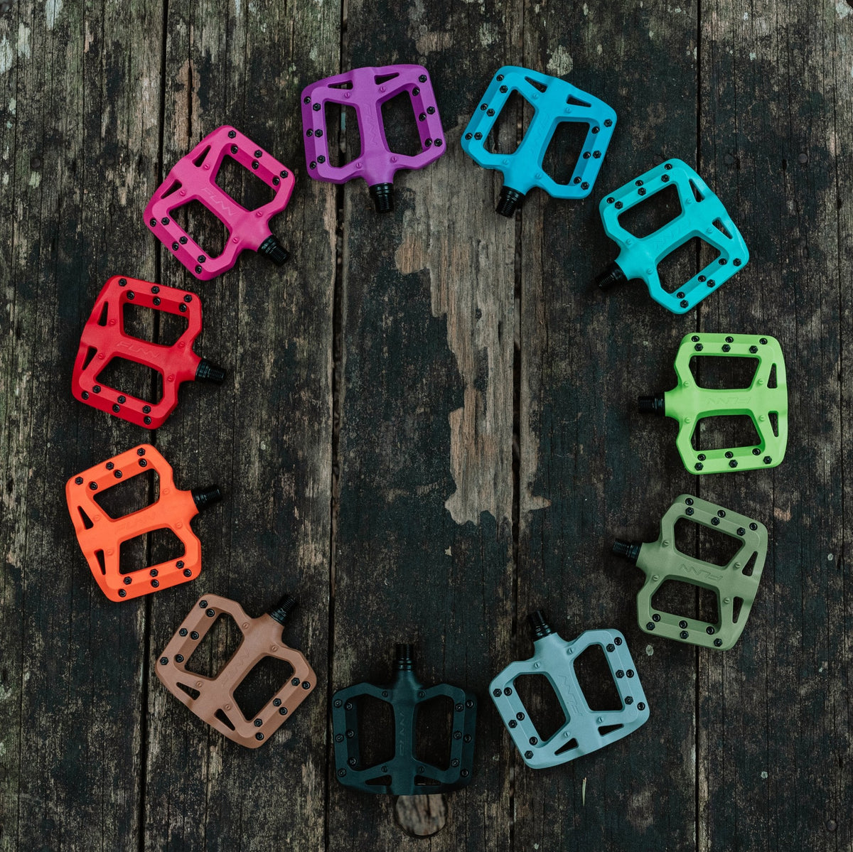 FUNN Taipan S Flat Pedals, colorful composite smaller platform for groms, arranged in a circle on rustic wood background