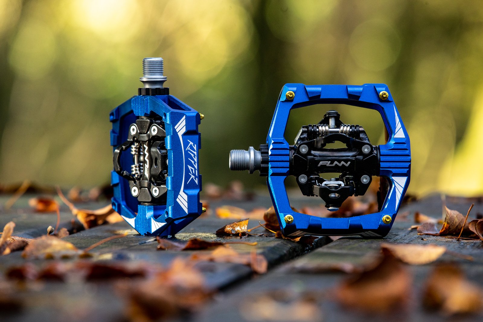 a pair of blue funn ripper clipless bike pedals on a wooden table with fallen leaves around