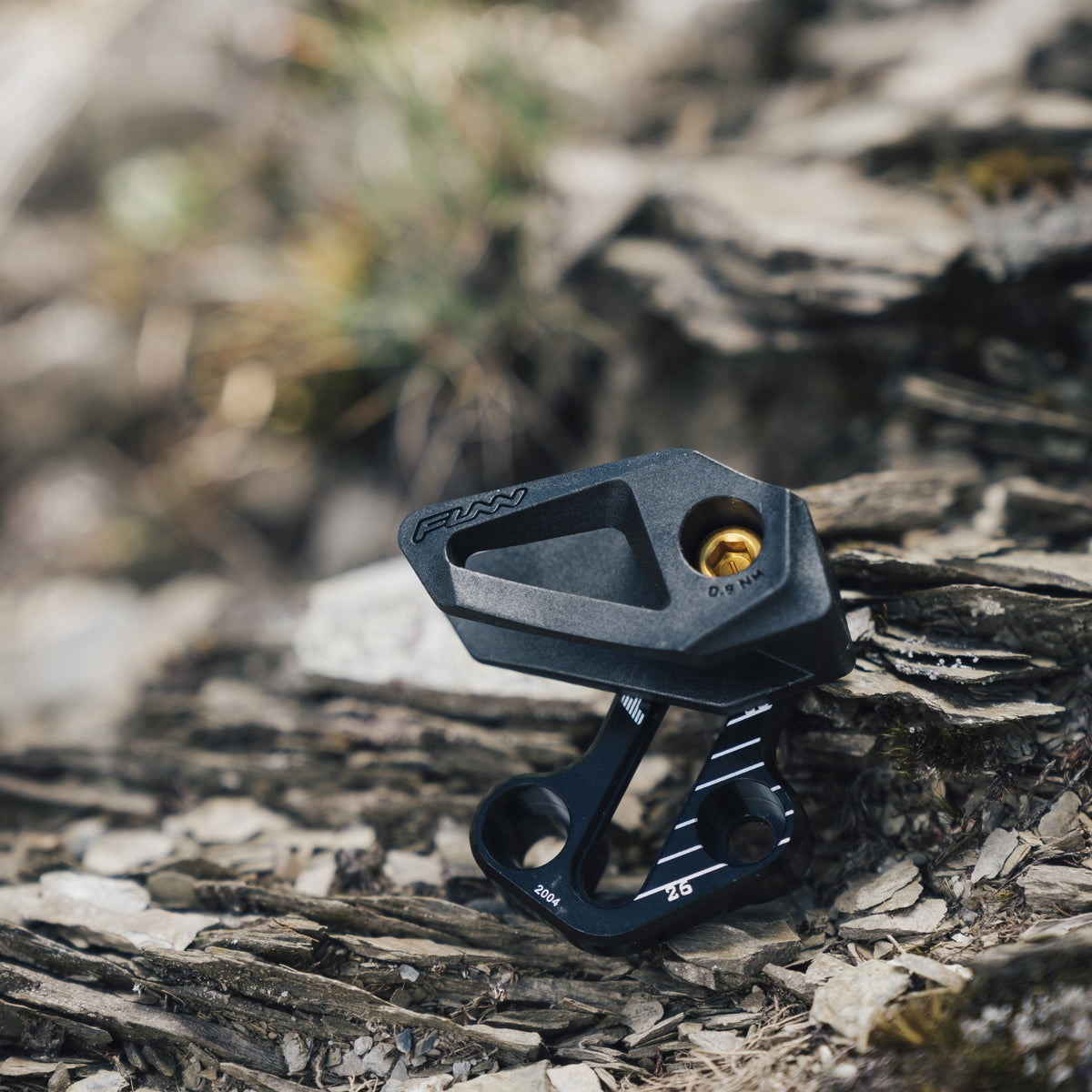 FUNN Zippa Lite E-Type Chain Guide, black alloy MTB chain retention device with gold bolt, shown on rocky trail surface