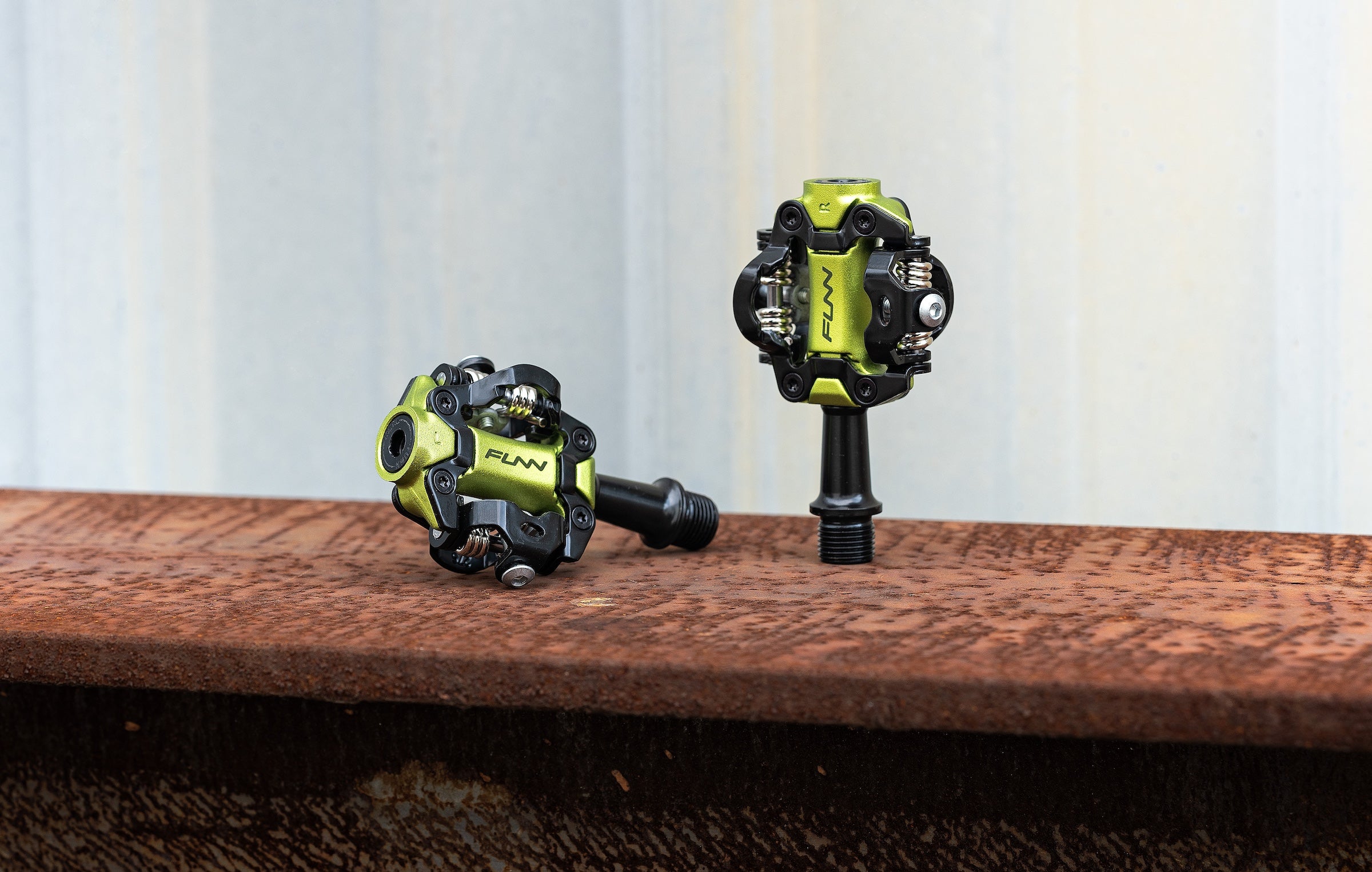 Funn Tactic clip-in pedals in green color, shown as a pair with one pedal standing upright and the other lying on its side on a rusted metal surface.