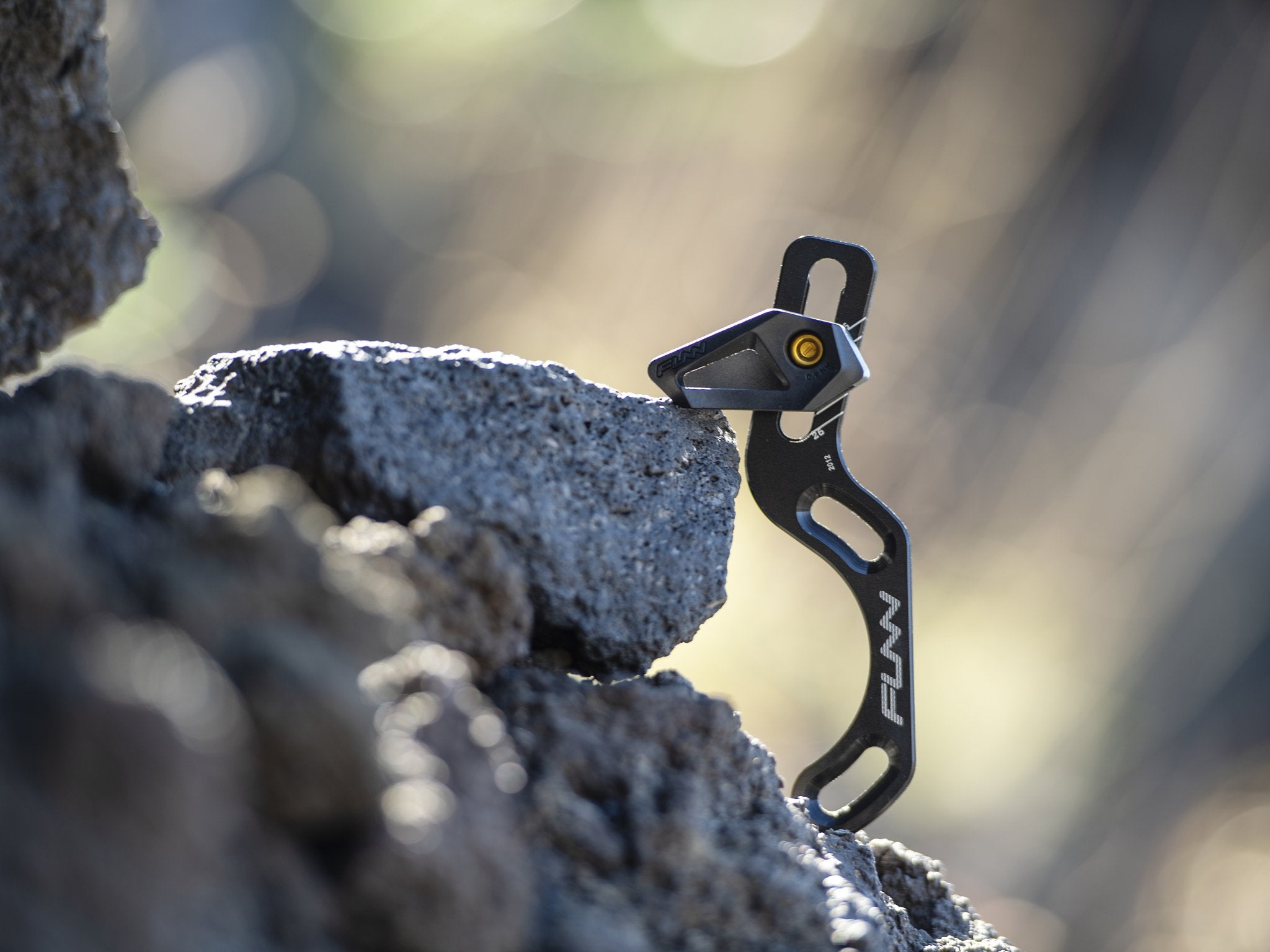 A Funn zippa lite iscg05 chain guide is displayed perched on a rough, rocky surface with a blurred background, highlighting its sleek design and sturdy construction.