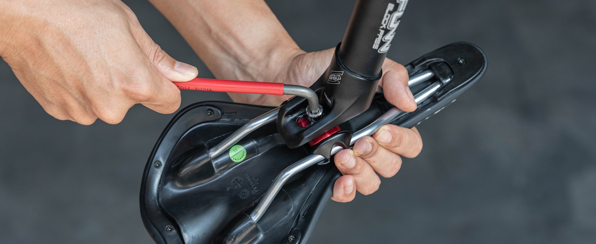 This image shows a person tightening a saddle onto a seat post using an Allen key.slider_item_nEKeyV