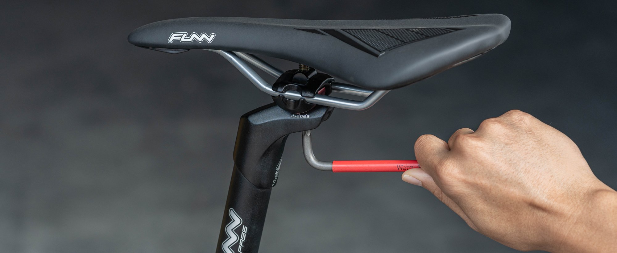 The image shows a person adjusting the funn blockpass seat post for positioning the funn skinny bike saddle using a hex key.slider_item_jYF7rt