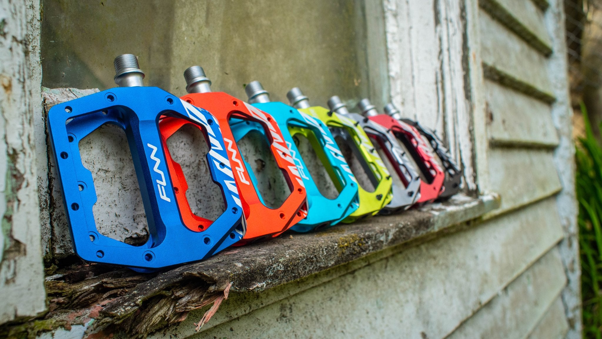 7 colours of funn funndamental flat bike pedals lining up along with the side of window