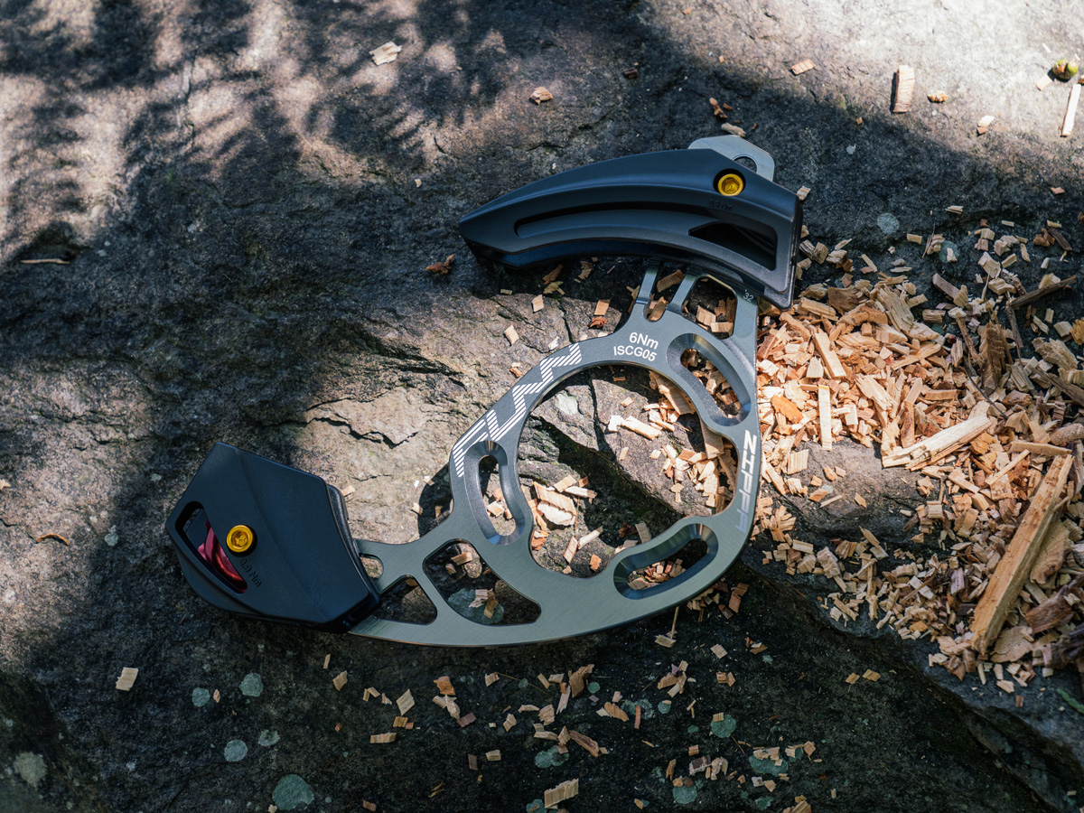 A gray Funn Zippa AM Mountain Bike Chain Guide is laying on a rock in the woods.