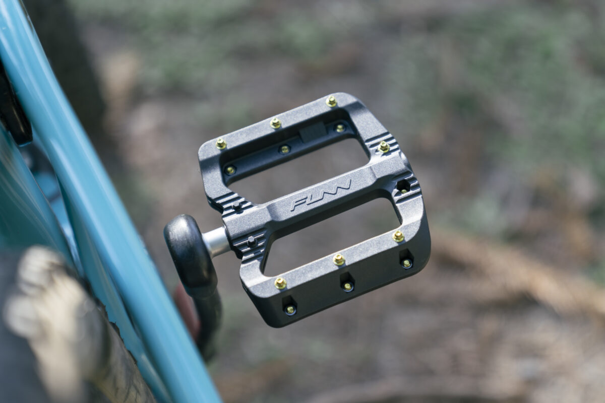 A close up of the pedals on a blue bike.