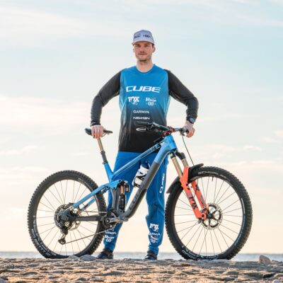 A man standing next to a blue mountain bike on the beach.