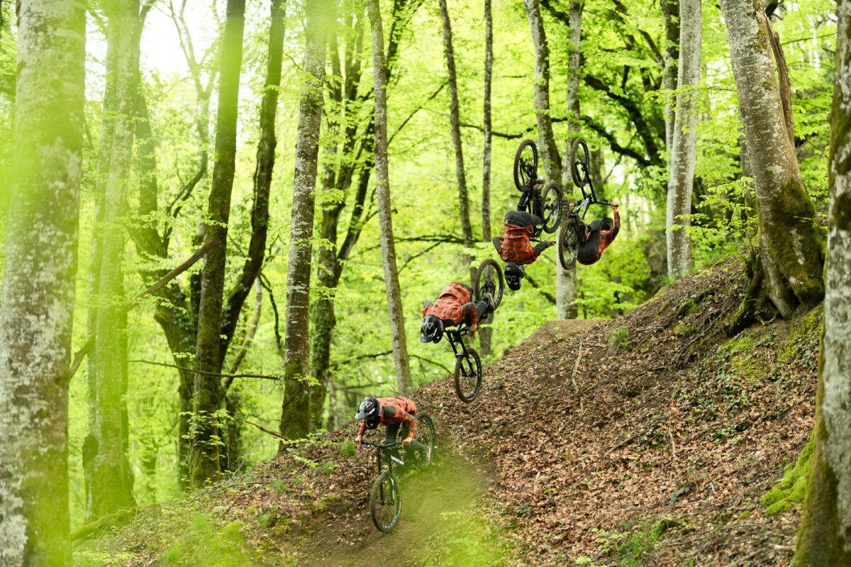 A group of mountain bikers riding down a trail in the woods.