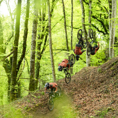 A group of mountain bikers riding down a trail in the woods.