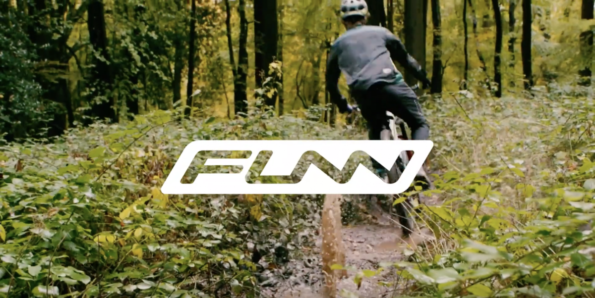 Funn rider on trail heading towards forest splashing up murky water with Funn logo at the center