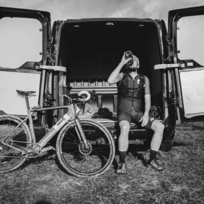 A man sitting in front of a van with his bike.