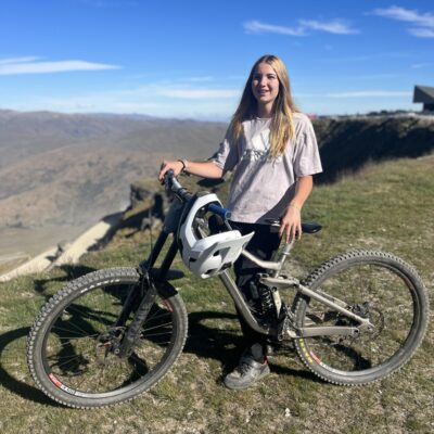 A girl with a mountain bike standing on top of a hill.
