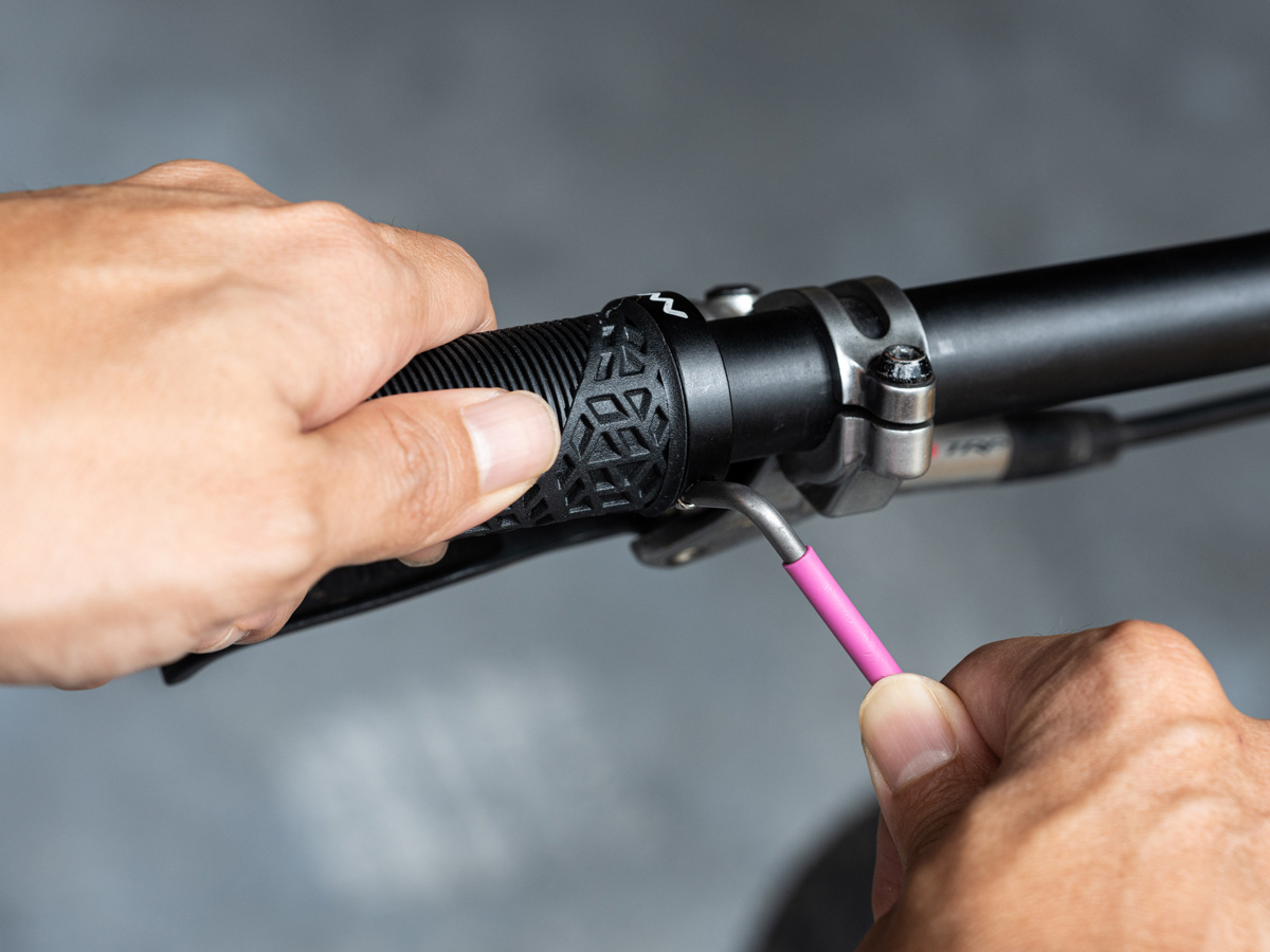 A person is using a pink tool to adjust the handlebars on a bike.