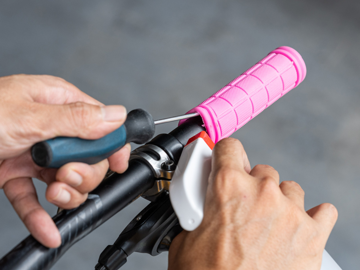 A man is removing a pink handlebar grip on a bicycle.